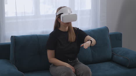 Frau-Mit-HMD-Display-Auf-Dem-Kopf-Sitzt-Auf-Der-Couch-In-Der-Wohnung-Und-Gestikuliert-Mit-Den-Händen,-Moderne-Technologie-Der-Virtuellen-Realität
